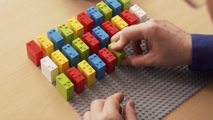 A keyboard layout made with colorful LEGO bricks placed on a grey LEGO baseplate. Each brick represents a letter or symbol, including accented characters, in a visually organized grid.