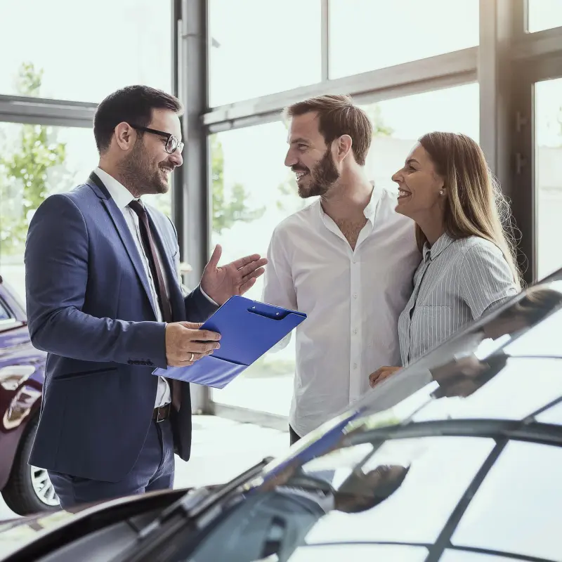 Junges Paar im Autohaus unterhält sich mit dem Autoverkäufer Junges Paar im Autohaus unterhält sich mit dem Autoverkäufer