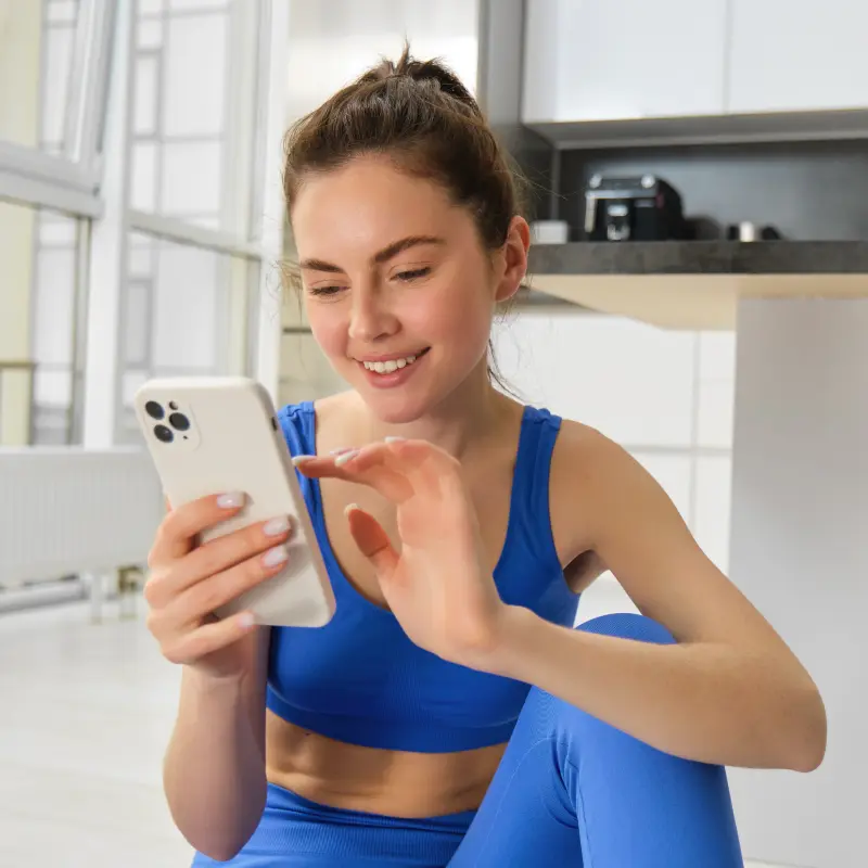 Eine junge Frau in Sportbekleidung schaut auf ihr Handy und lächelt Eine junge Frau in Sportbekleidung schaut auf ihr Handy und lächelt