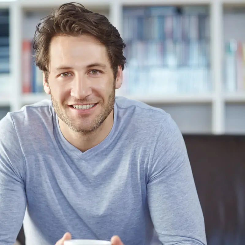 Ein junger Mann sitzt mit einer Tasse Kaffee auf dem Sofa Ein junger Mann sitzt mit einer Tasse Kaffee auf dem Sofa