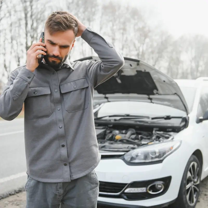 BarmeniaGothaer Versicherung Schaden melden: Ein junger Mann telefoniert. Im Hintergrund ist ein kaputtes Auto BarmeniaGothaer Versicherung Schaden melden: Ein junger Mann telefoniert. Im Hintergrund ist ein kaputtes Auto