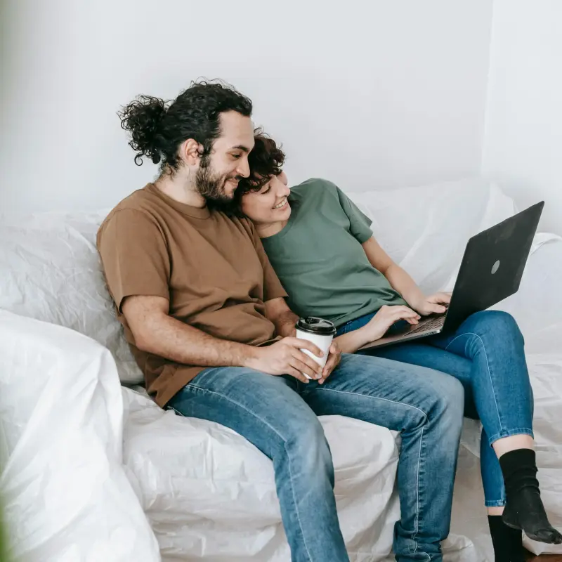 Ein Paar sitzt auf einer Couch und schaut auf ein Laptop. Ein Paar sitzt auf einer Couch und schaut auf ein Laptop.