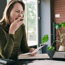 Photo of a person in green top yawning at a desk, signifying sleep deprivation, which increases the density of synapses.