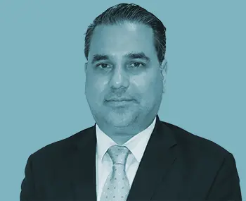 A man in a suit and tie poses for a formal portrait against a plain blue background.