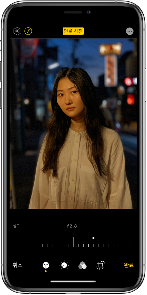 인물 사진 모드 사진의 편집 화면. 화면 왼쪽 상단에 있는 조명 강도 버튼 및 심도 조절 버튼. 화면 상단 중앙에 인물 사진 버튼이 켜져 있고 오른쪽 상단에 플러그인 버튼이 있음. 사진이 화면 중앙에 있고 사진 아래에는 심도 조절 설정을 조절할 수 있는 슬라이더가 있음. 슬라이더 아래에는 왼쪽에서 오른쪽으로 취소, 인물 사진, 조절, 필터, 자르기 및 완료 버튼이 있음.