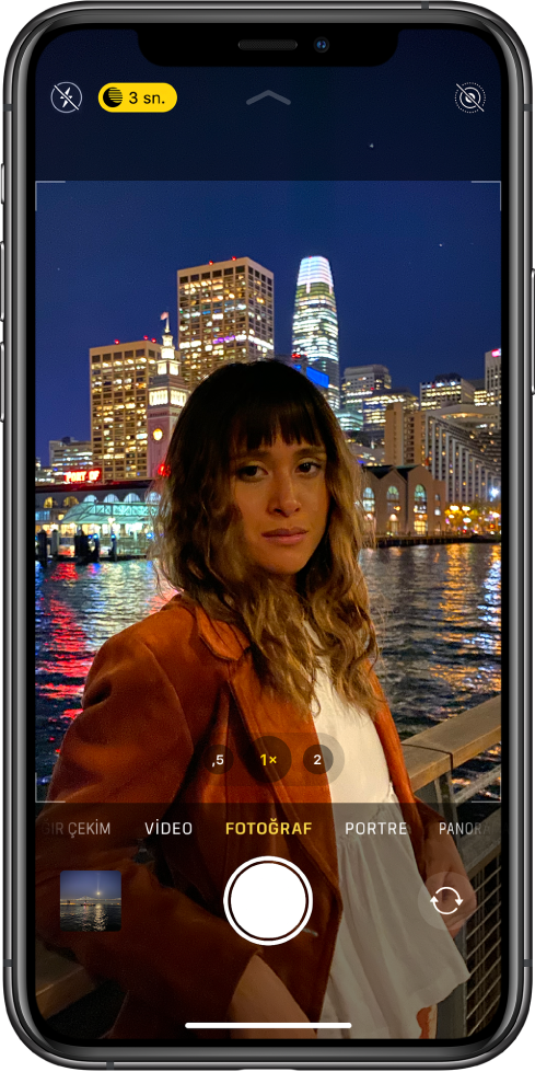 Fotoğraf modunda Kamera. Flaş ve Gece modu düğmeleri ekranın sol üstünde görünüyor. Flaş düğmesi kapalı ve Gece modu düğmesi etkin. Live fotoğraf düğmesi sağ üst köşededir. Fotoğraf ve video görüntüleyici sol alt köşede. Deklanşör düğmesi alt ortadır ve kamera seçici düğmesi sağ alt köşede.