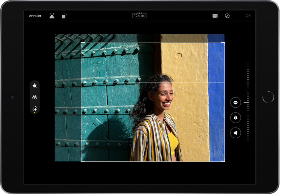 L’iPad en orientation paysage. Au centre de l’écran se trouve une photo en mode édition avec une grille en superposition et un cadre pour recadrer l’image. Sur le côté gauche de l’écran se trouvent les boutons Ajuster, Filtres et Recadrer ; le bouton Recadrer est sélectionné. Sur le côté droit de l’écran se trouvent les options d’amélioration du recadrage et le curseur d’intensité. Dans le coin supérieur gauche se trouvent les boutons Annuler, Retourner et Pivoter. Dans le coin supérieur droit se trouvent les boutons Proportions, Annoter et OK.