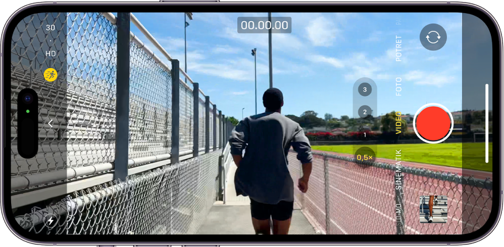 iPhone diputar secara horizontal. Kamera dibuka dan dalam mode Video. Di bingkai kamera, seseorang sedang joging. Tombol Kilat berada di pojok kiri bawah layar. Tombol Kontrol Kamera ada di bagian kiri tengah layar. Di pojok kiri atas terdapat ubah cepat untuk mengalihkan resolusi dan laju bingkai video. Tombol Tindakan di pojok kiri atas dinyalakan. Di sisi kanan terdapat, dari atas ke bawah, tombol Belakang Pemilih Kamera, tombol Rekam, serta tombol Penampil Foto dan Video. Dalam jendela bidik, seseorang berlari.
