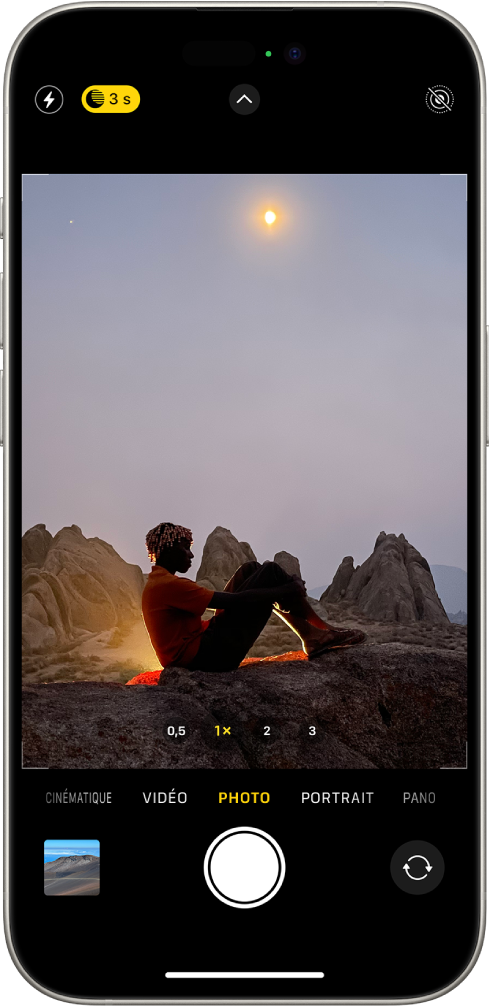 L’écran « Appareil photo » en mode Photo. Une scène de nuit apparaît dans le viseur. Les boutons correspondant au flash et au mode Nuit s’affichent dans l’angle supérieur gauche de l’écran et le mode Nuit est activé. Le bouton « Commandes de l’appareil photo » se trouve en haut au centre et le bouton « Live Photos » dans le coin supérieur droit. En bas de l’écran, de gauche à droite, se trouvent le bouton « Visualiseur de photos et vidéos », le bouton « Prendre une photo » et le bouton « Sélecteur de caméra - face arrière ».