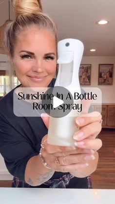 a woman holding a bottle in her hand and pointing to it with the words sunshine in a bottle room spray