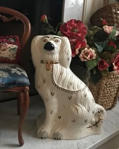 a white dog statue sitting next to a chair and flowers