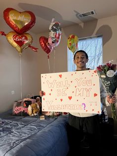 a woman holding up a sign that says will you be my valentine? with balloons in the background