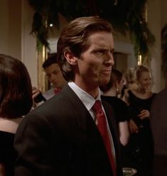 a man in a suit and red tie standing next to other people at a party