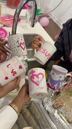 several people holding up cups with the word jesus on them and hearts painted on them