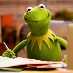 kermie the frog sitting at a desk with a notepad and pen in his hand