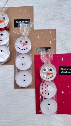some white candles are wrapped in plastic and have snowman faces on them with red ribbon