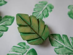 two green leaves are sitting on a white tablecloth with green leafy designs in the background