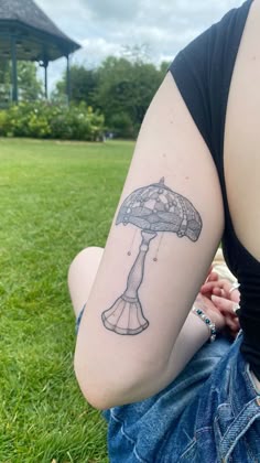 a woman sitting in the grass with a tattoo on her arm, holding an umbrella