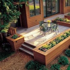 a wooden deck with raised planters on it and an outside dining area in the background