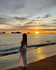 a beautiful woman standing on top of a beach next to the ocean at sunset or dawn