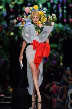 a woman walking down a runway with flowers in her hair