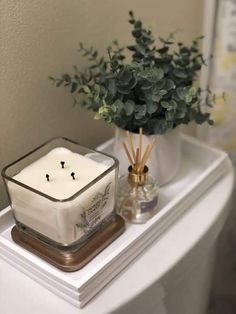 a white candle sitting on top of a bathroom counter next to a potted plant