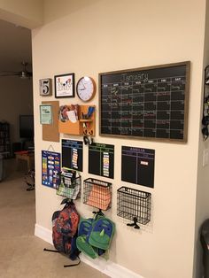 several backpacks are hanging on the wall in front of a chalkboard and clock