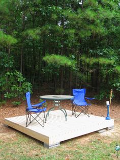 two chairs and a table on a wooden platform in the middle of a wooded area