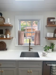 a kitchen sink sitting under a window next to a counter top with dishes on it