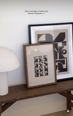 two framed pictures sit on a wooden shelf next to a white lamp and mushroom lamp
