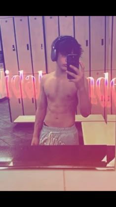 a man wearing headphones is looking at his cell phone in front of a mirror