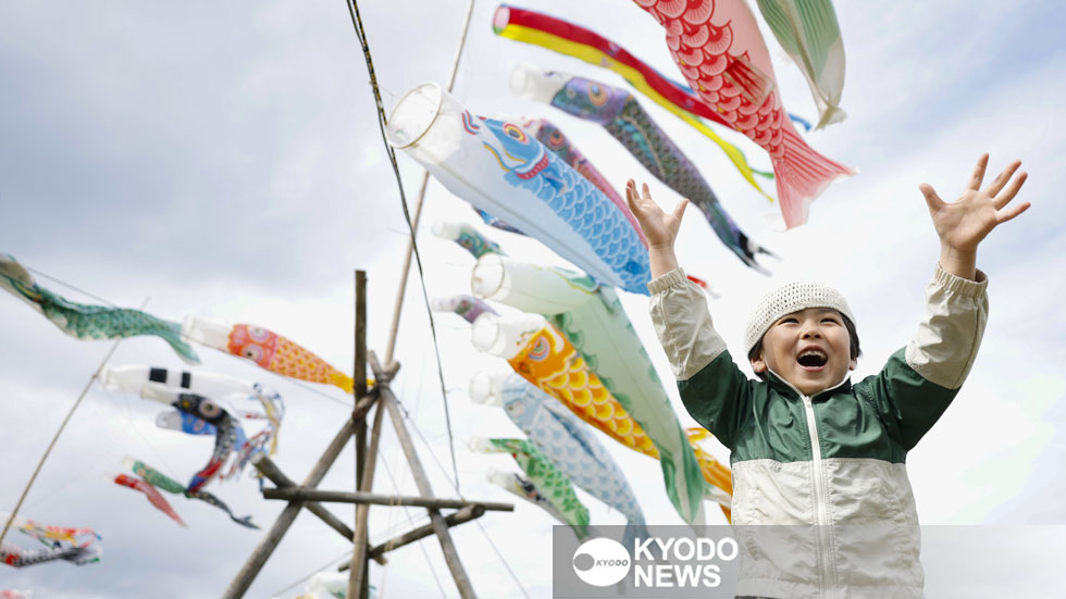 風に舞う色とりどりのこいのぼりと男の子=2026年5月、石川県珠洲市大谷地区