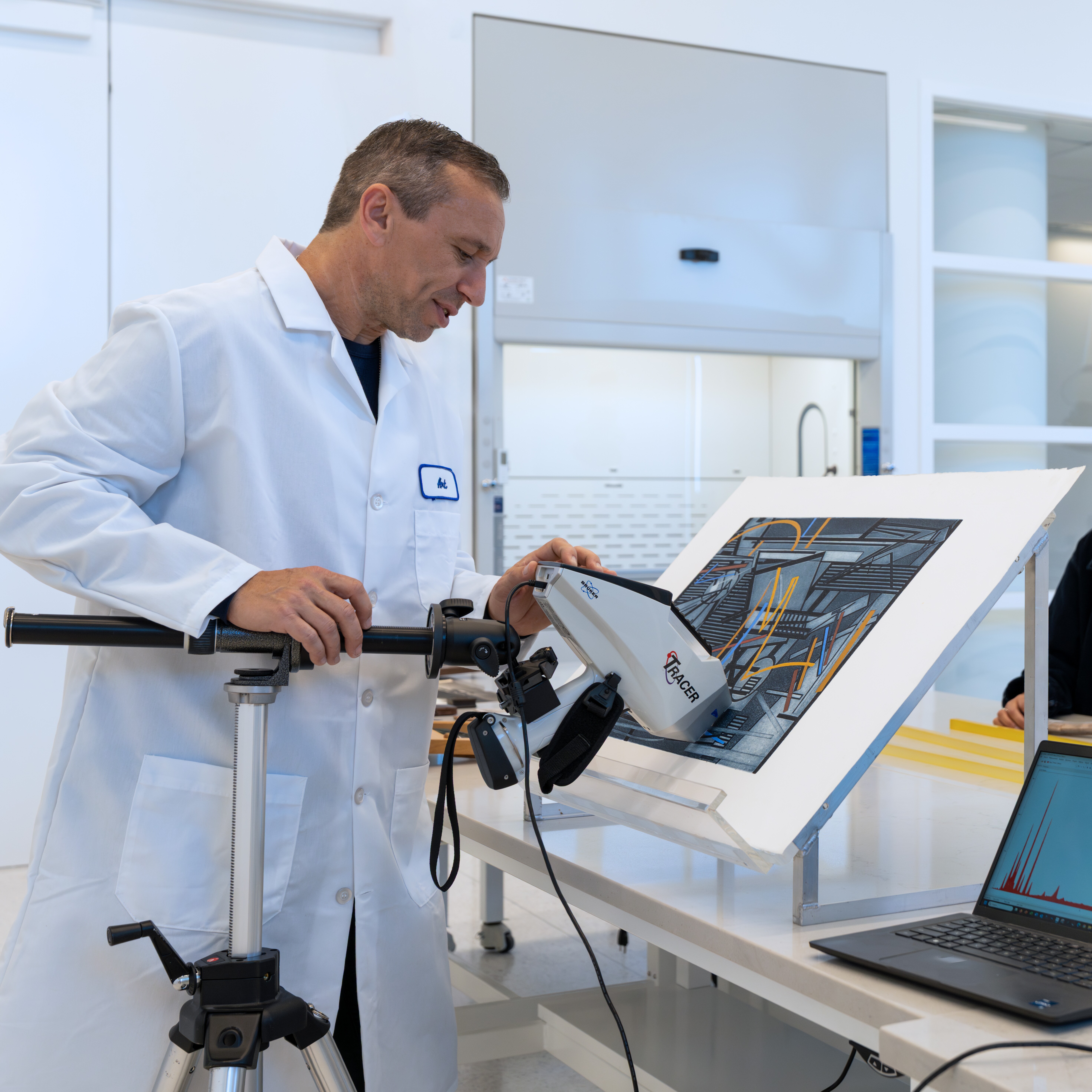People in lab coats use scientific instruments in a large, clean laboratory environment