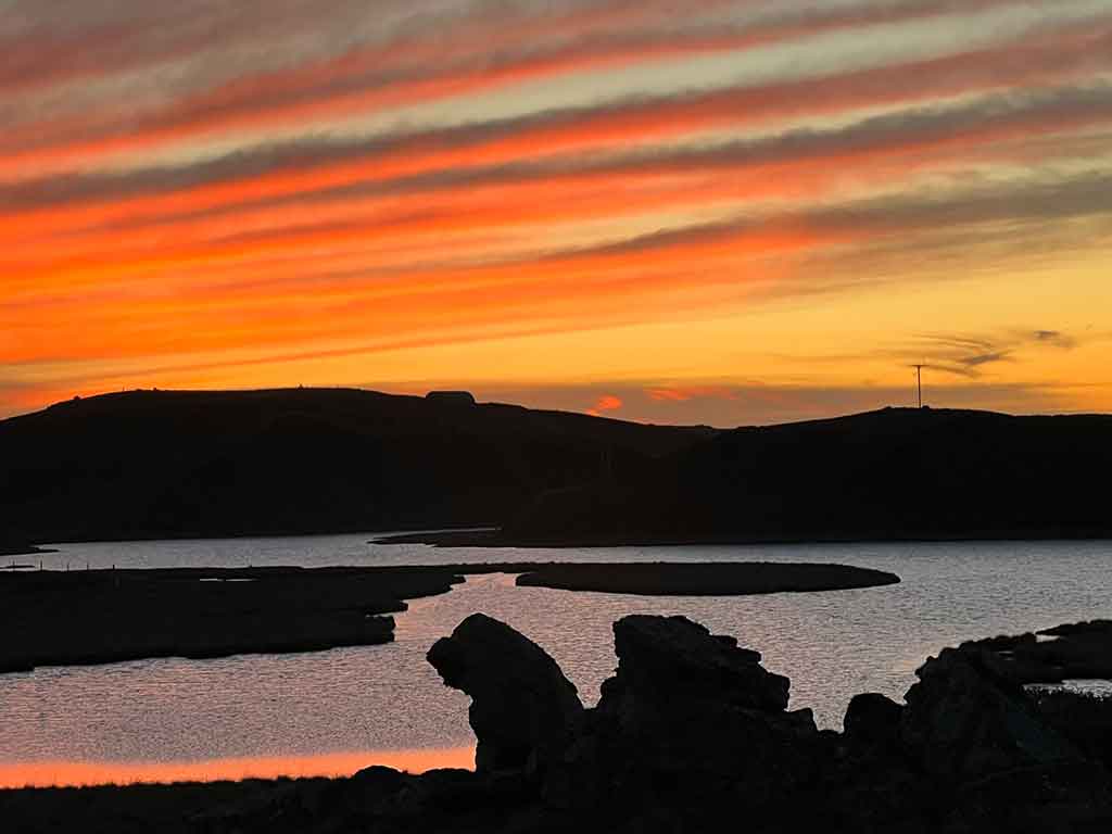 HOME 22 The silhouette of rocks by a loch with a peach, pink sunset