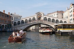 A white bridge, covered with a roof, passing over a canal with buildings on both sides.