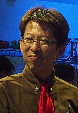 Kensuke Tanabe, a Japanese man wearing glasses, a brown shirt, and red tie