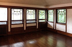 One of the bedrooms on the third floor. The room has wooden floors, a sloping ceiling, and windows with geometric patterns.