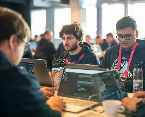 Several developers programming around a table with laptops and beverages at a Software Defined Vehicle Hackathon event.